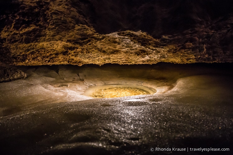 Small pool of water surrounded by rock and ice.