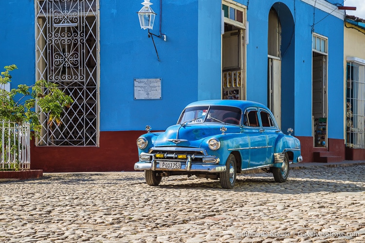 Blue classic car on a cobbled street with a blue building in the background.