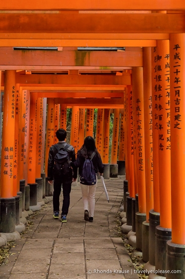 Young couple walking in the torii gate tunnel at Fushimi Inari shrine, Kyoto