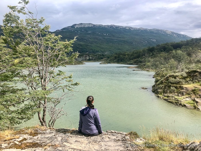 Woman sitting on a small cliff looking at Lapataia River.