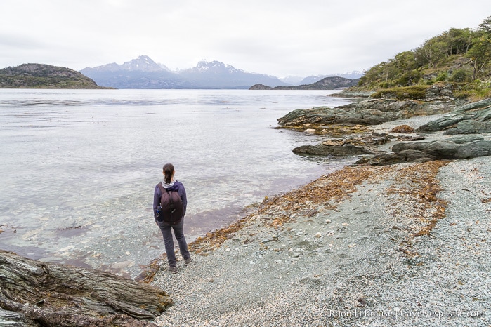 Woman standing on the beach looking out at the bay and mountains.