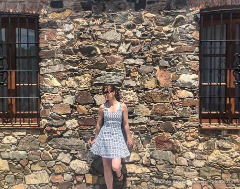 Standing against the stone wall of a building.