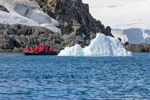 A zodiac cruising along the shoreline and past a small iceberg.
