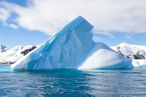 Iceberg floating in front of snow covered hills.