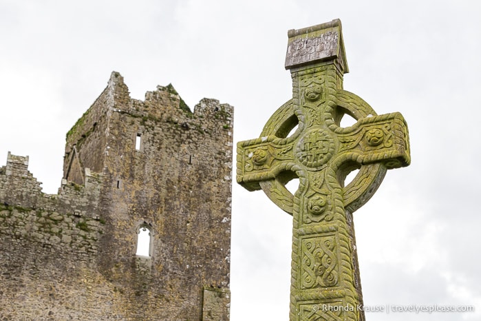 Engraved stone cross with ruins in the background.