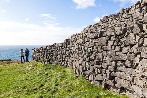 People looking at the ocean at the end of a stone wall at Dún Aonghasa.