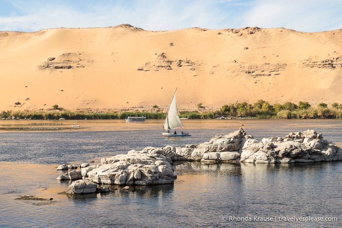Felucca sailing on the Nile past a sand dune.
