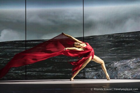 Dancer arching back and holding her red dress as it blows behind her in the wind.