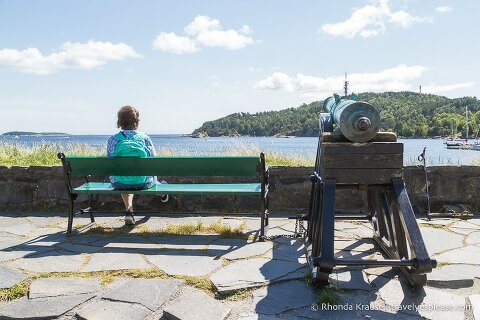 Woman sitting on a bench beside a canon looking out on the harbour.