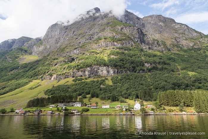 Small village on the shoreline of Nærøyfjord with a towering mountain in the background.