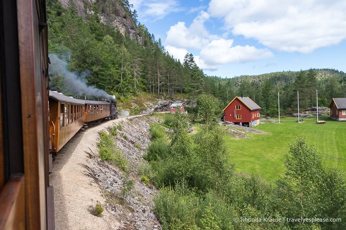 The train coming up alongside a red building.