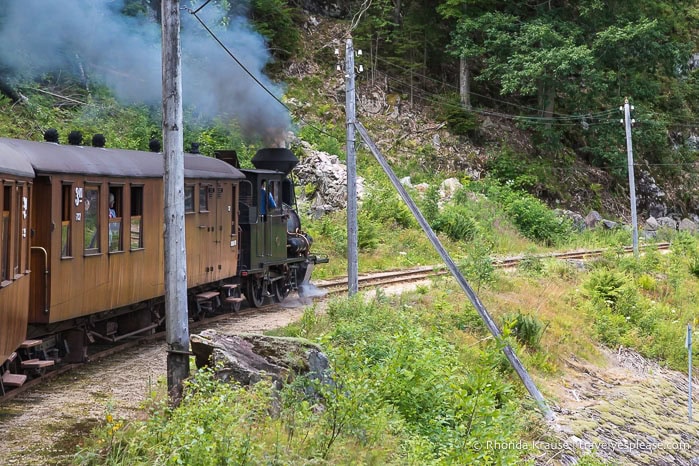 Steam engine puffing black smoke as it pulls the rail cars.