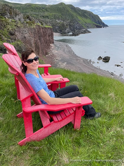 Woman sitting in a red chair with cliffs and a beach in the background.