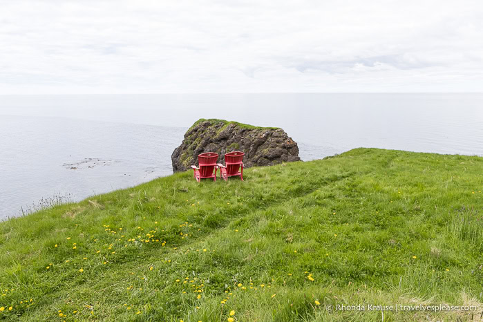 Pair of red chairs in a clifftop meadow by the sea.