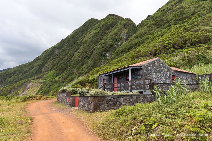 Stone house with tall green cliffs in the background. 