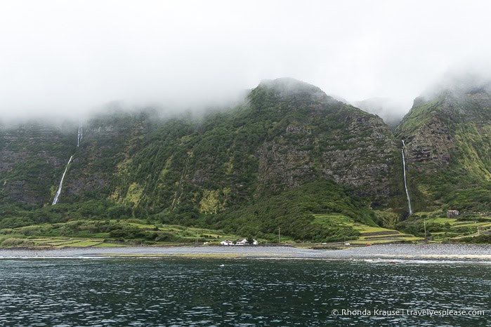 Waterfalls flowing down a mountain beside the ocean.